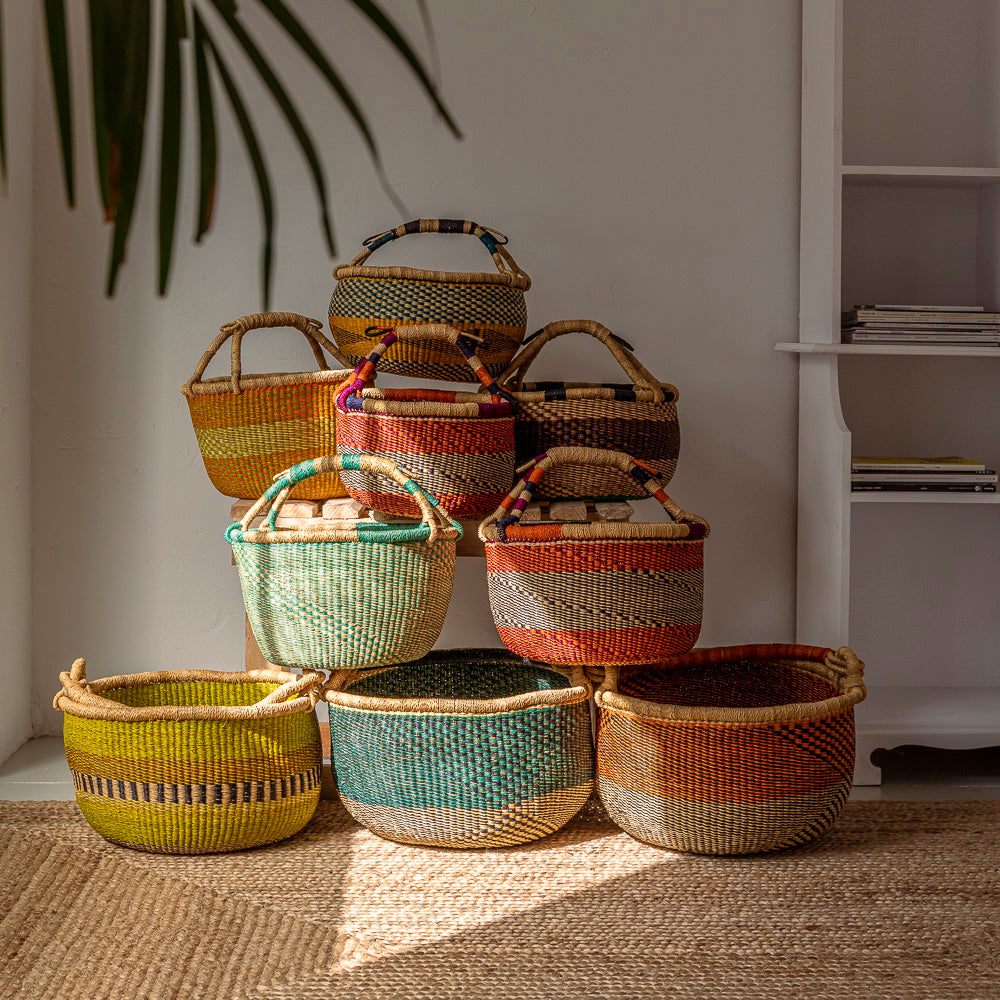 A stack of market baskets in various colours on a rattan rug.  Designed by Akan Republic.