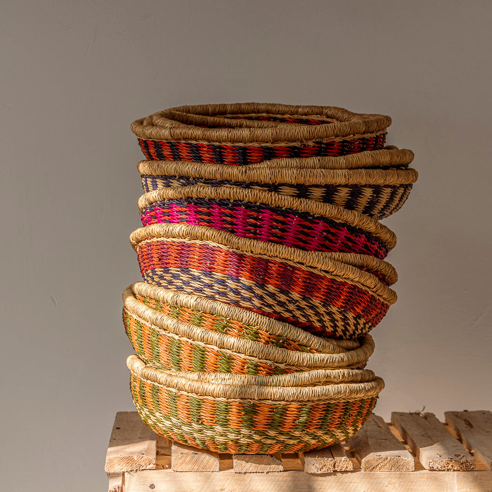 A vertical stack of small baskets in various colours on a wooden bench. These baskets were designed by Akan Republic.